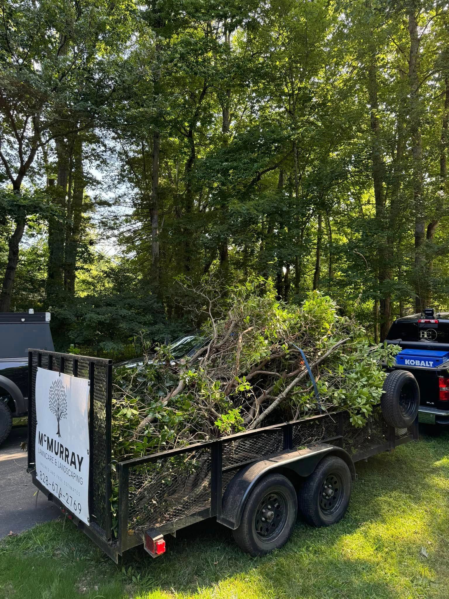 A trailer filled with branches and leaves is parked next to a truck.
