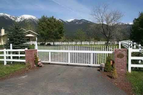 A white fence surrounds a driveway with mountains in the background.