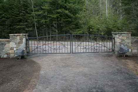 A wrought iron gate is surrounded by stone pillars and trees.