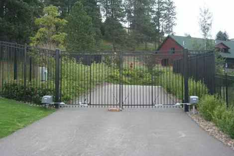 A black gate is closed on a driveway leading to a house.