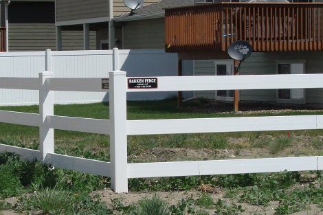 A white fence surrounds a grassy area with a house in the background