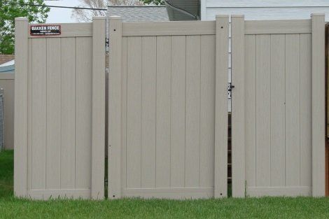A white fence with a gate is sitting in the grass in front of a house.