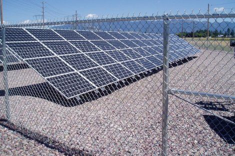A chain link fence surrounds a field of solar panels.