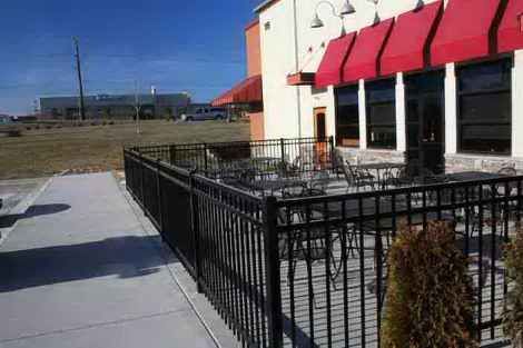A restaurant with a patio and tables and chairs behind a fence.