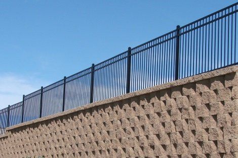 A fence surrounds a brick wall with a blue sky in the background.