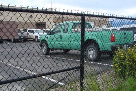 A green truck is parked behind a chain link fence