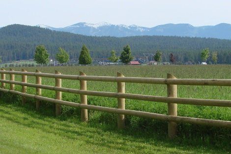 A wooden fence surrounds a grassy field with mountains in the background.