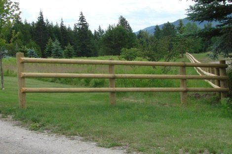 A wooden fence surrounds a grassy field with trees in the background