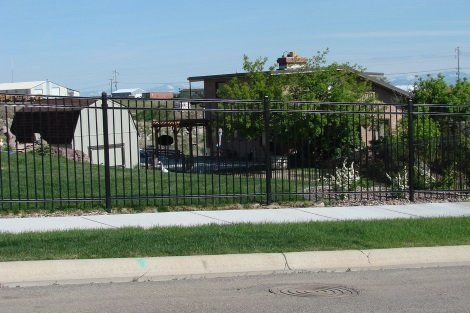 A metal fence surrounds a grassy area with a house in the background.