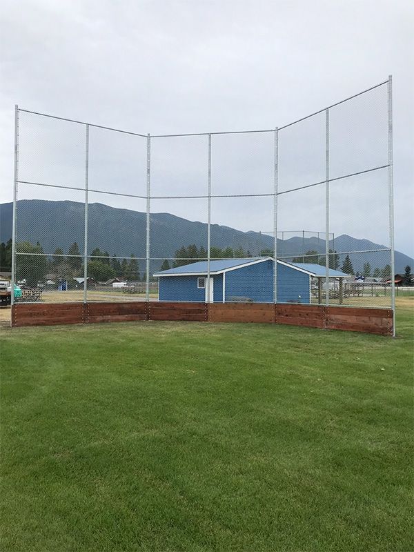 A baseball field with a fence and a blue building in the background.