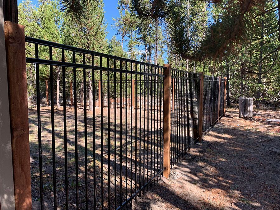A metal fence with a wooden post in the middle of a forest.