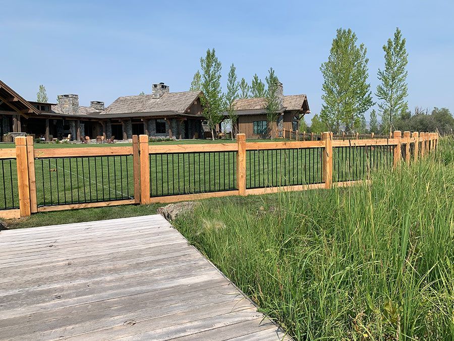 A wooden fence surrounds a large house in a grassy field.