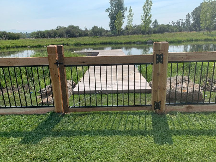 A wooden fence surrounds a pond with a dock in the background.