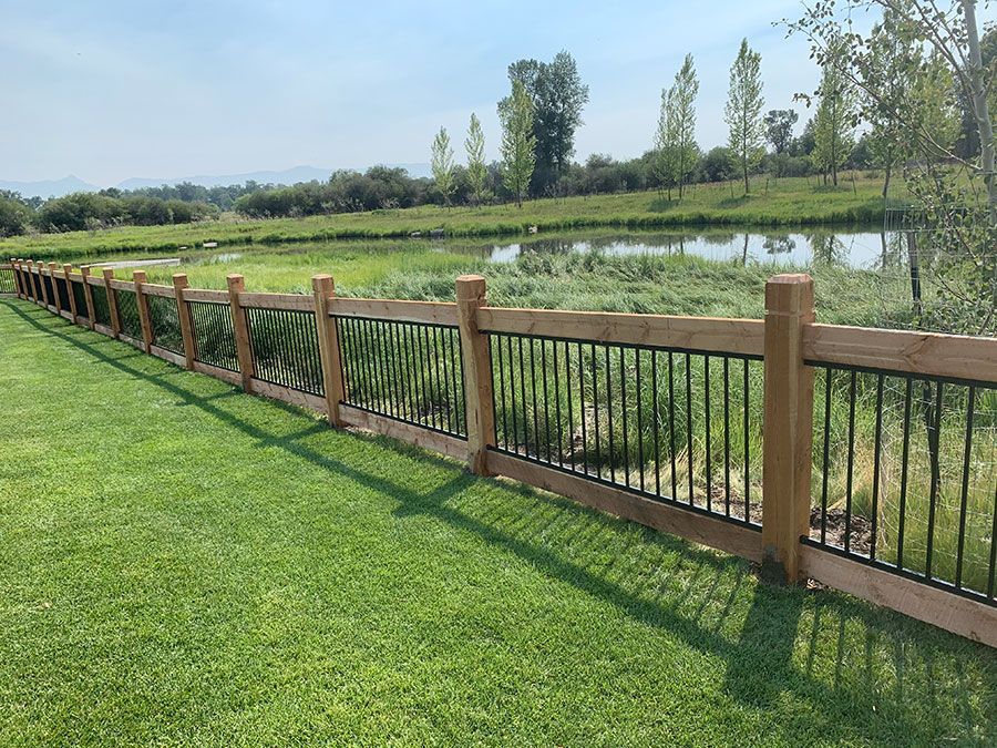 A wooden fence surrounds a lush green field with a pond in the background.