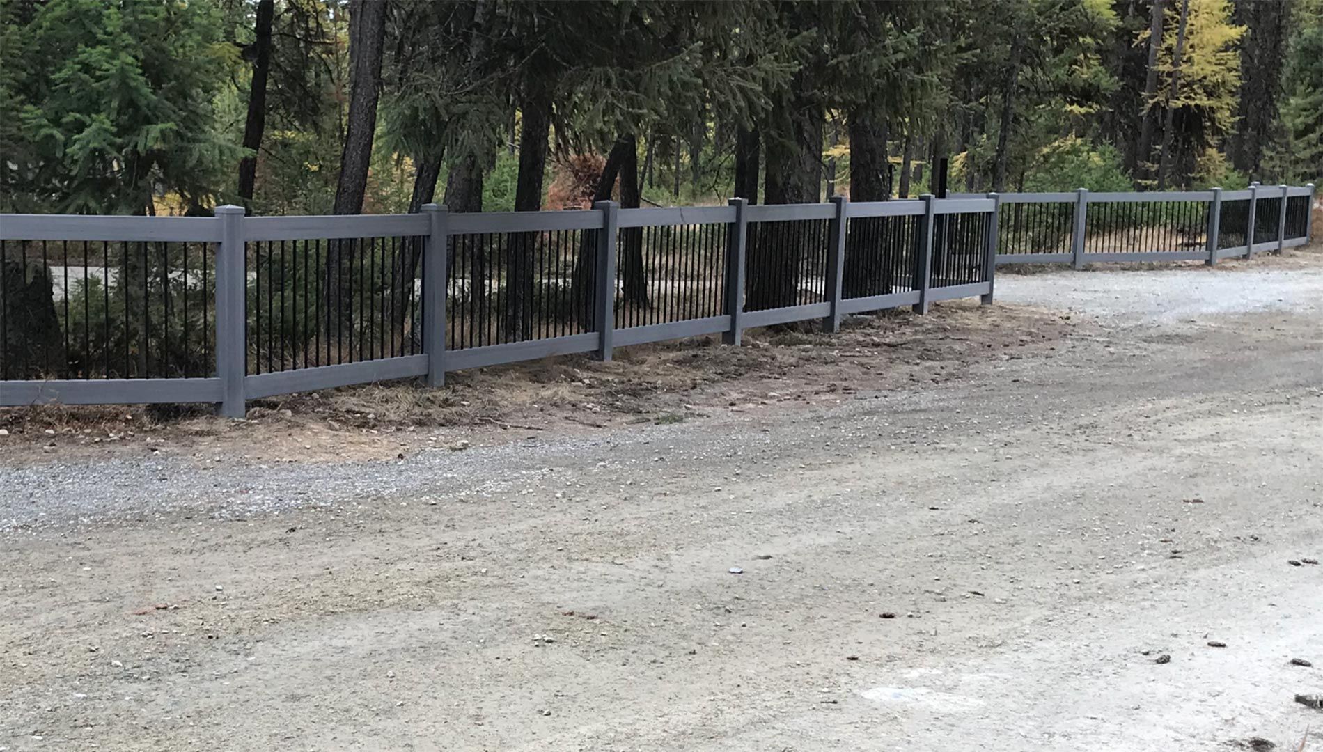 A wooden fence surrounds a gravel road in the woods.