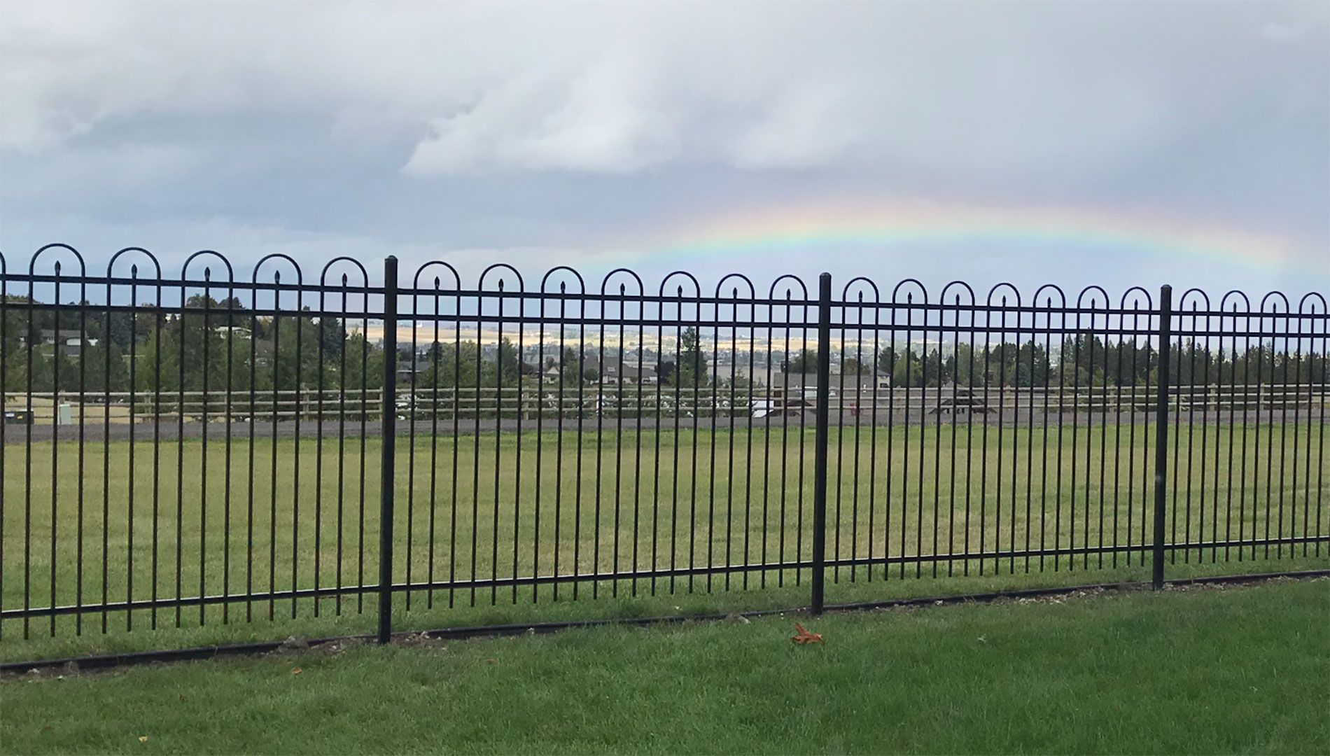 A fence with a rainbow in the sky behind it