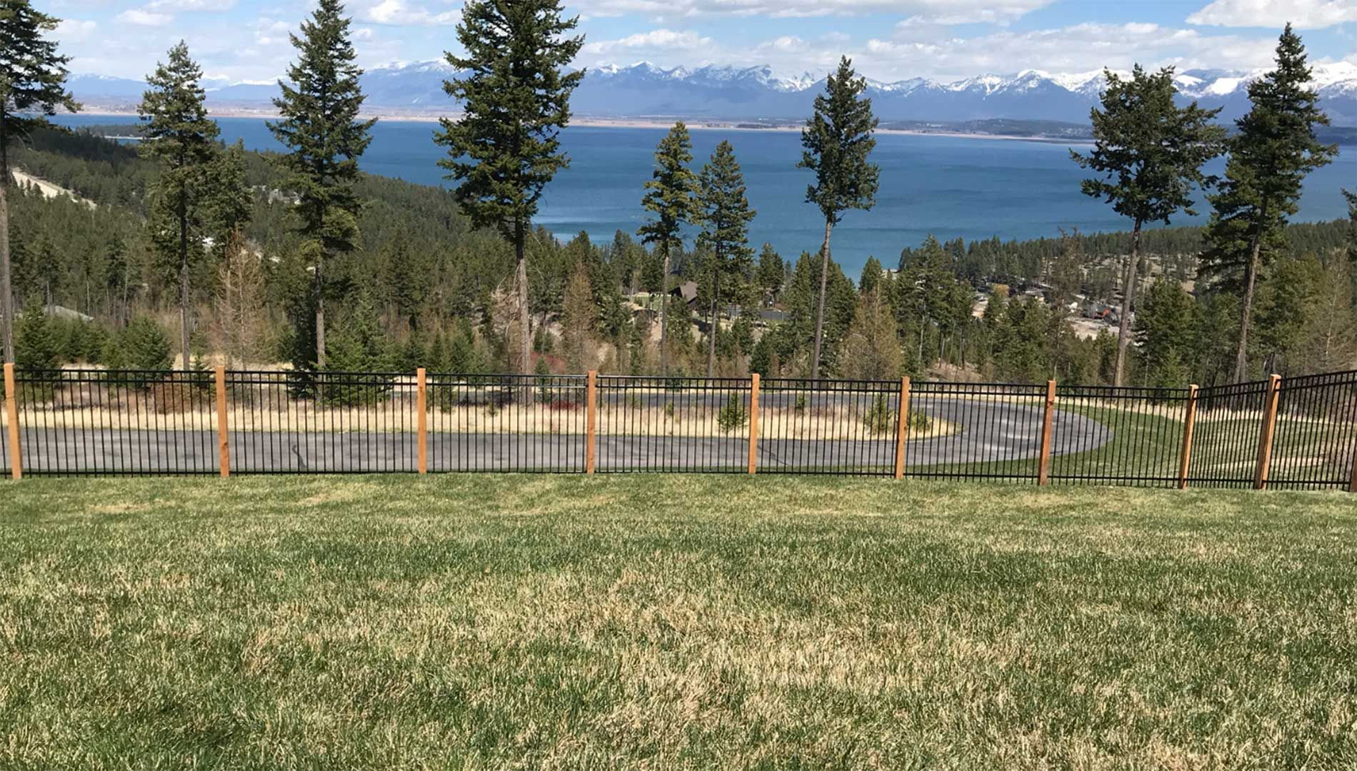 A fence surrounds a grassy field with a lake in the background.