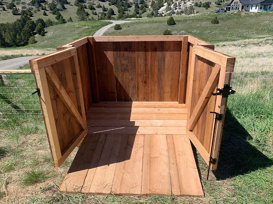A wooden shed with its doors open is sitting in the grass.