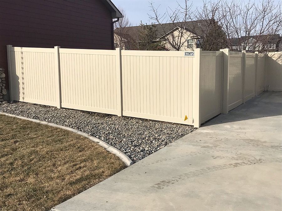 A white vinyl fence is sitting next to a concrete driveway.