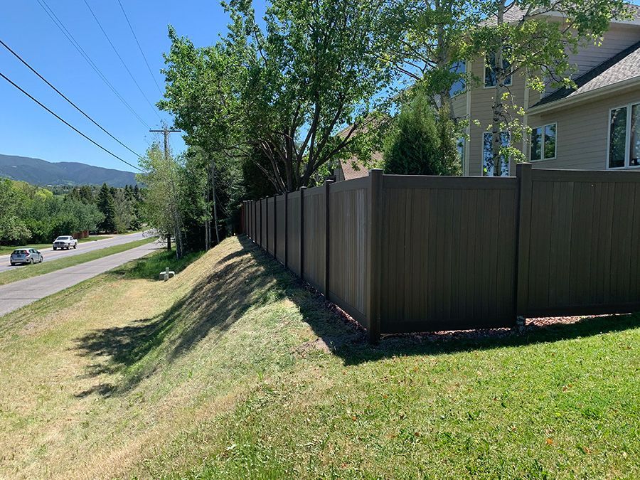 A long wooden fence surrounds a grassy hill next to a house.
