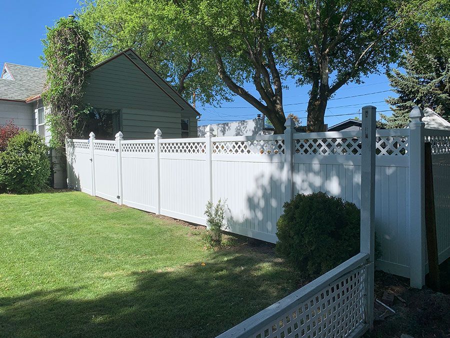 A white fence surrounds a lush green yard in front of a house.