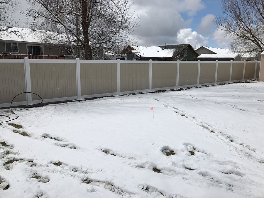 A white fence is surrounded by snow in a backyard.