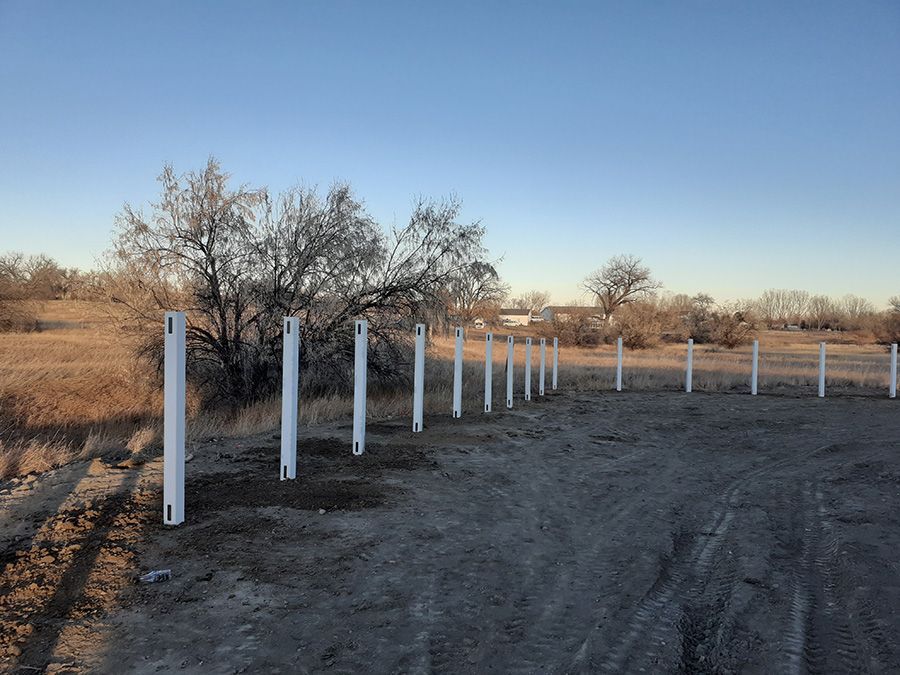A row of white fence posts in a dirt field.