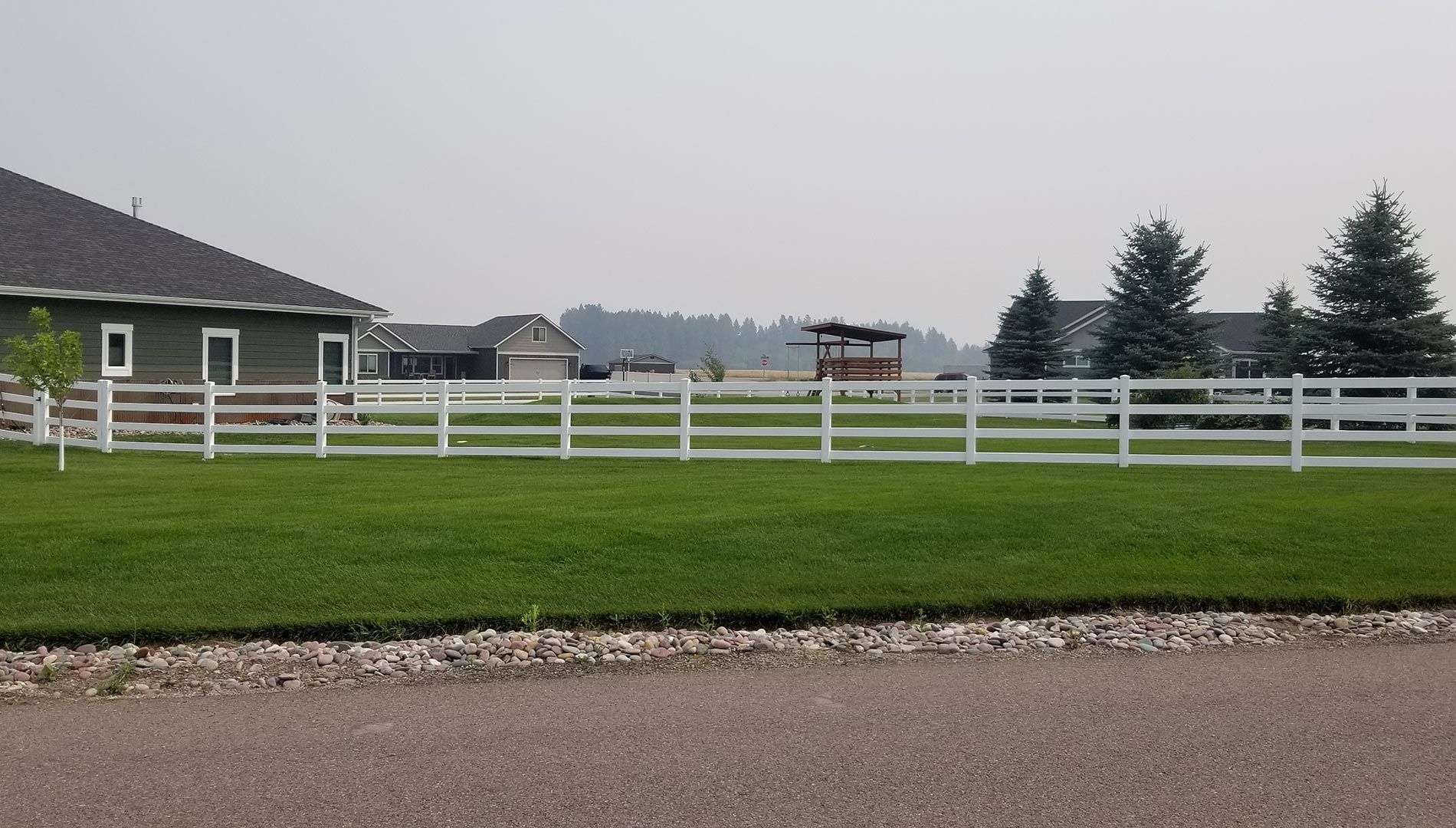 A white fence surrounds a lush green field in front of a house