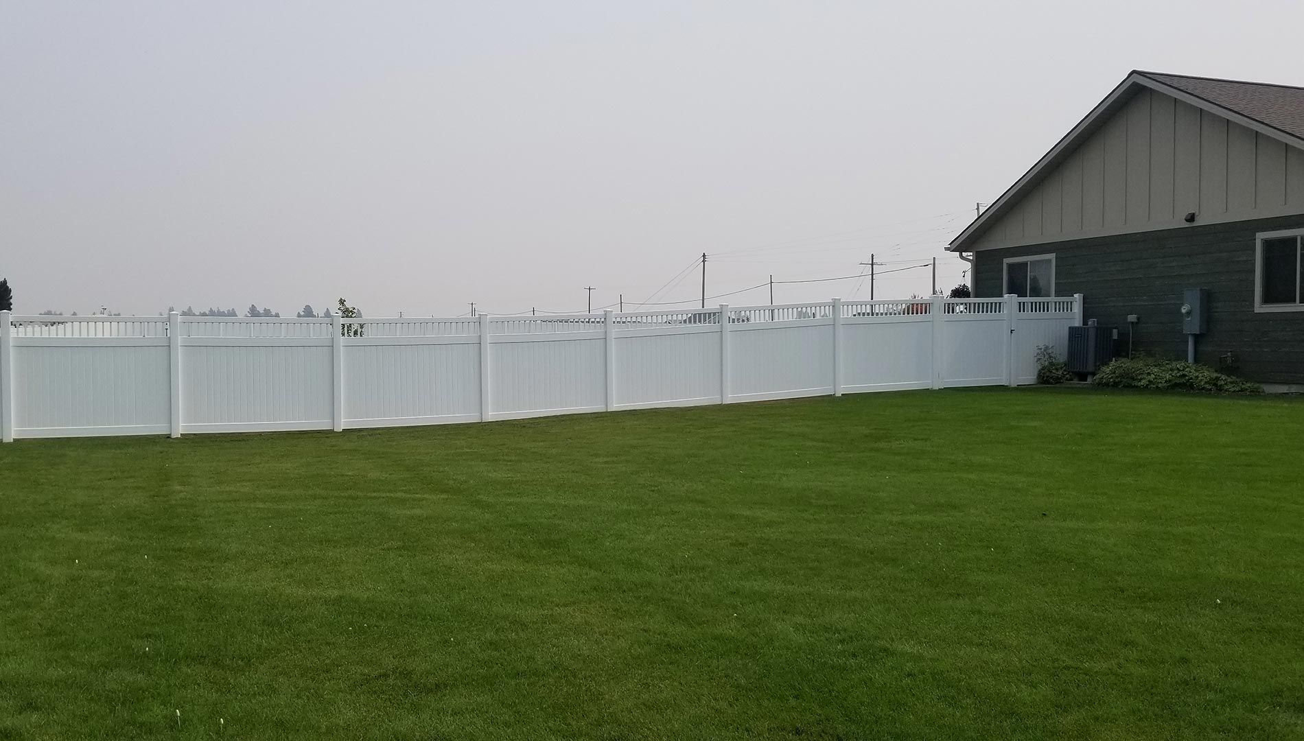 A white fence surrounds a lush green lawn in front of a house.