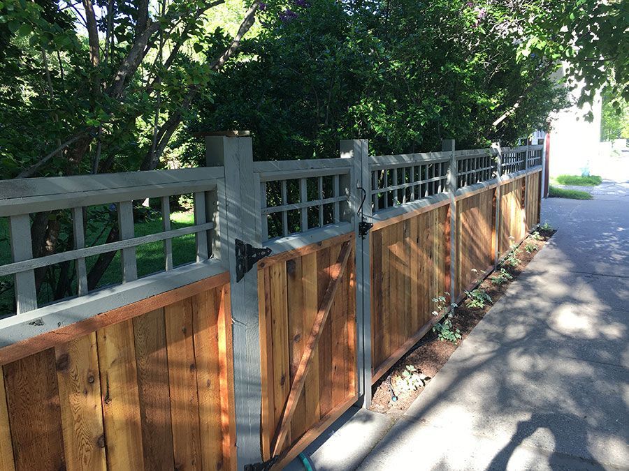 A wooden fence with a white gate is sitting on the side of a road.