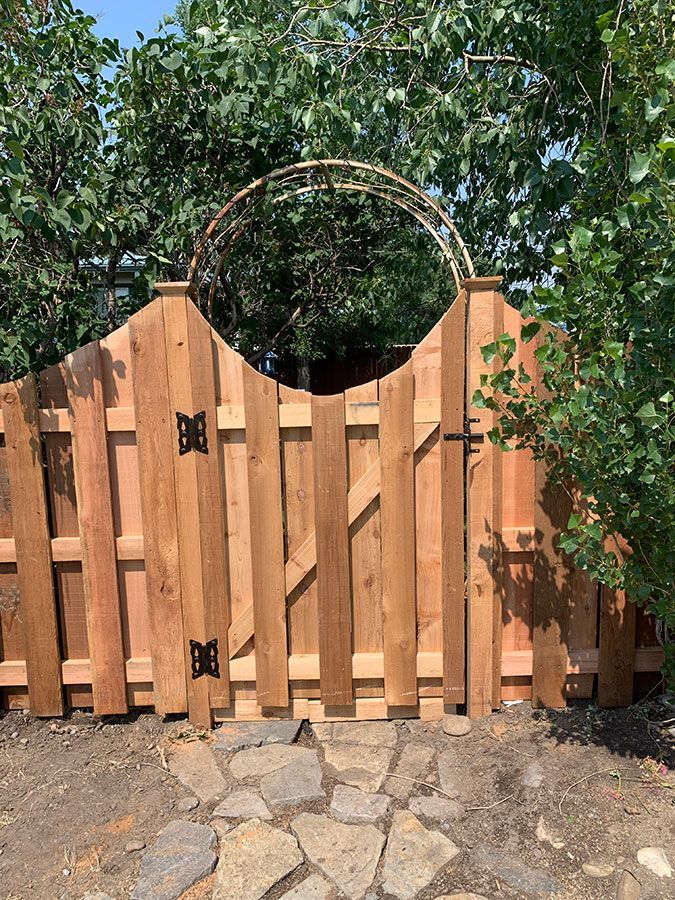 A wooden fence with a gate in the middle of it surrounded by trees.