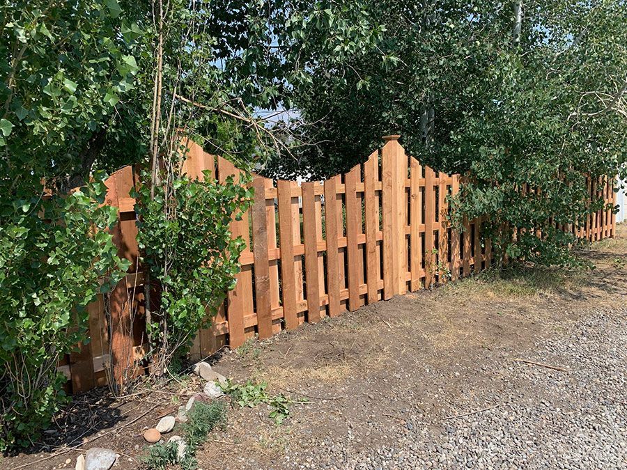 A wooden fence surrounded by trees and bushes on a gravel road.