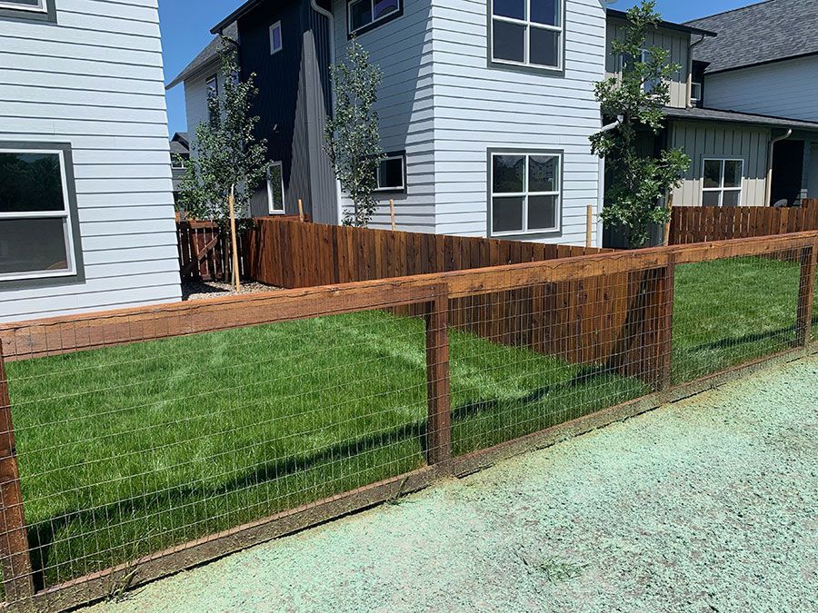 A wooden fence surrounds a lush green lawn in front of a house.