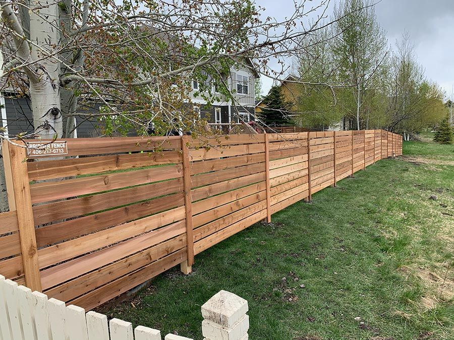 A wooden fence is surrounded by grass and trees in front of a house.
