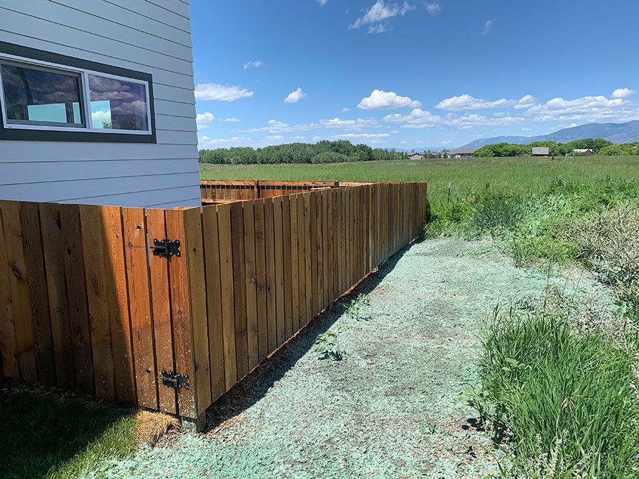 A wooden fence surrounds a grassy field next to a house.