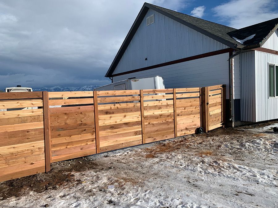 A wooden fence is sitting in front of a house in the snow.