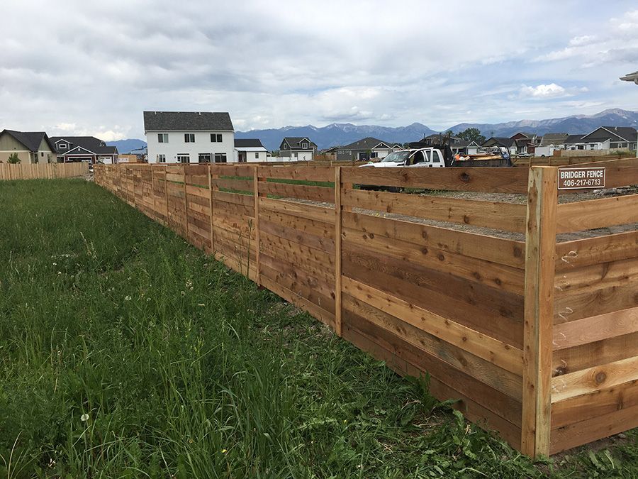 A long wooden fence surrounds a grassy field with a house in the background.