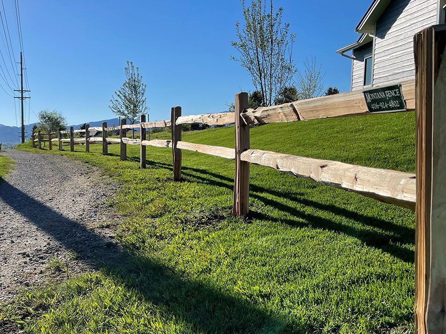 A wooden fence surrounds a grassy field next to a dirt road.