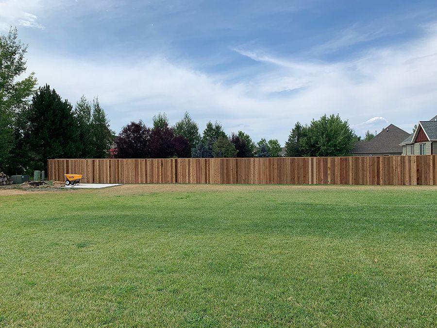 A wooden fence surrounds a large lush green field.