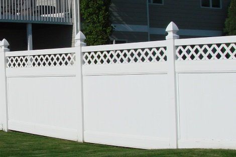 A white fence with a lattice design is in front of a house
