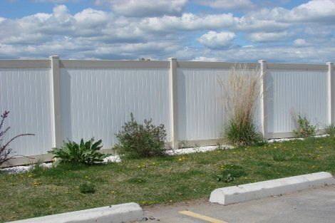 A white fence surrounds a grassy area in a parking lot