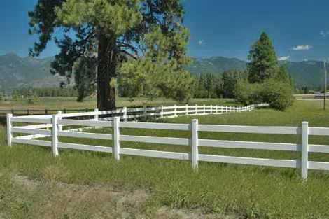 A white fence surrounds a grassy field with mountains in the background.
