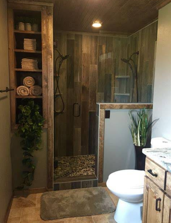 Rustic bathroom with wooden shower, built-in shelving, and toilet. Green and brown tones throughout, with a rug and plants.