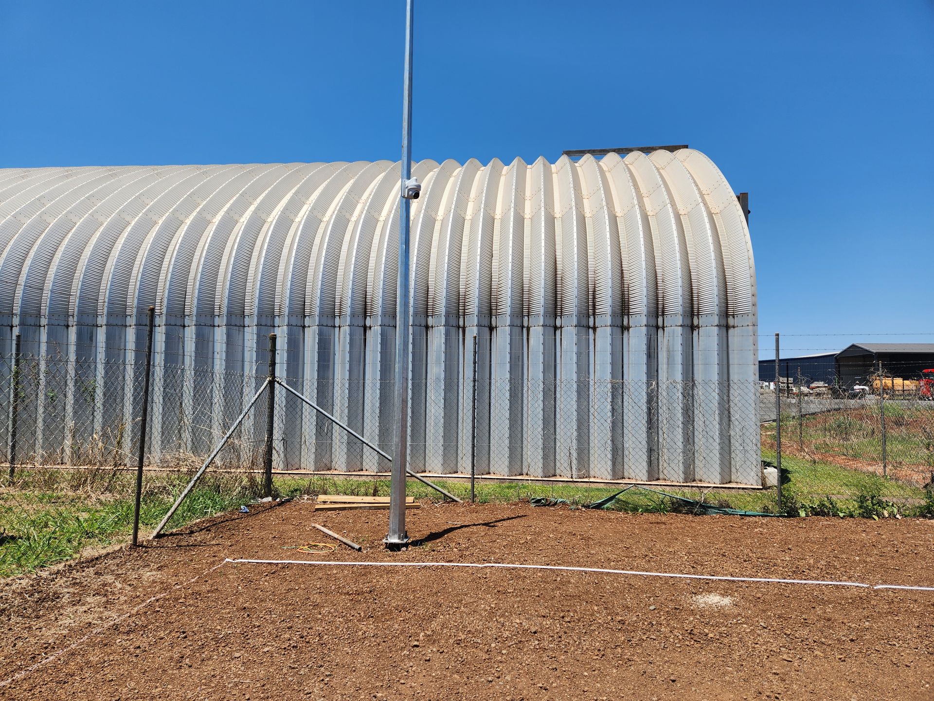 A curved, corrugated metal building stands behind a chain-link fence, with a tall metal pole in the foreground Tableland Self Storage In Atherton, QLD