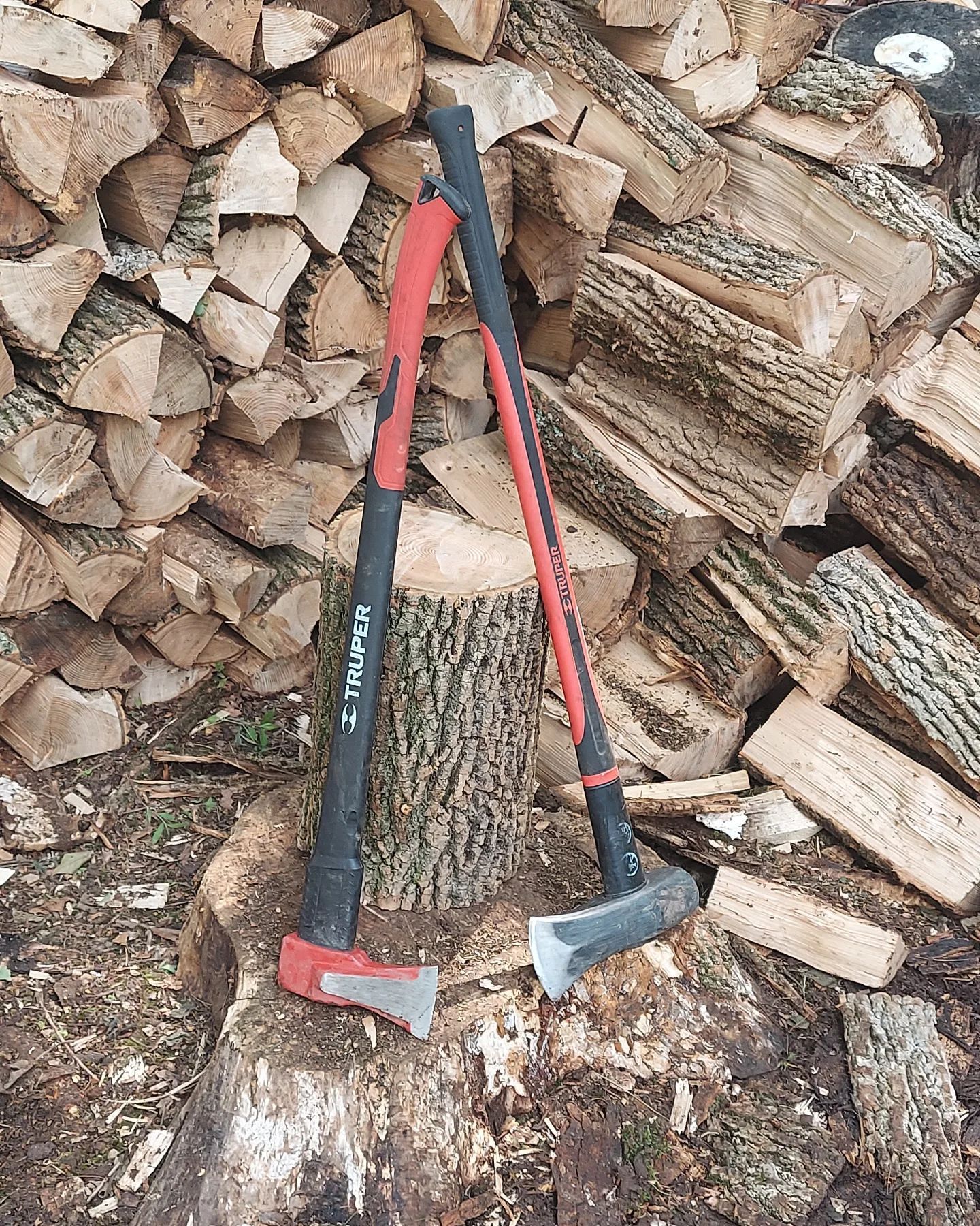 Two axes with red and black handles rest on a pile of split firewood.