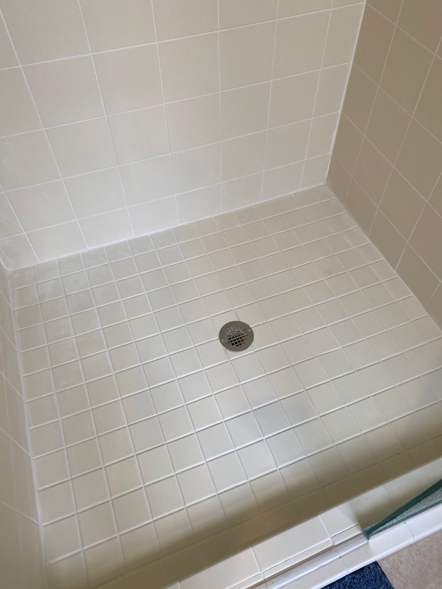 A shower stall with white tiles and a drain.