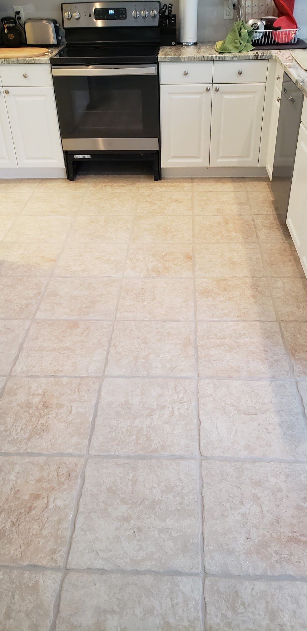 A kitchen with white cabinets , a stove , and a tile floor.