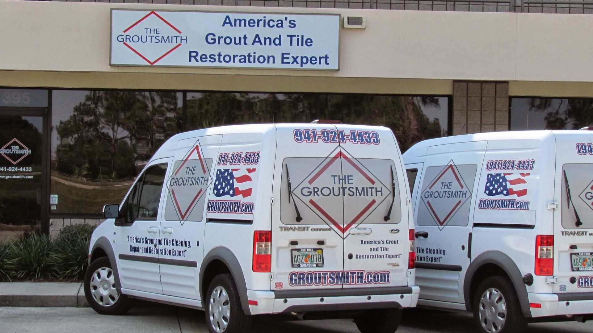 Three white vans are parked in front of a building that says america 's grout and tile restoration expert
