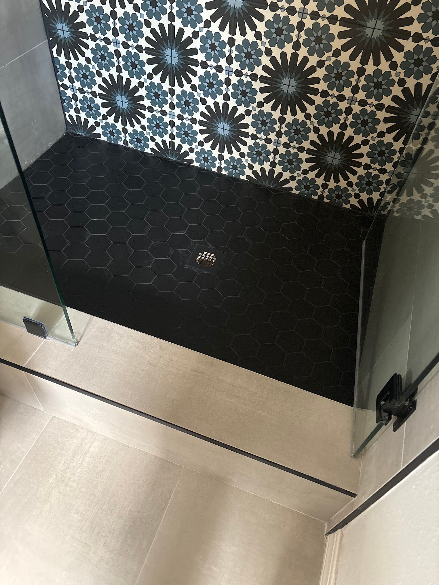 A shower stall with a black tile floor and a glass door.