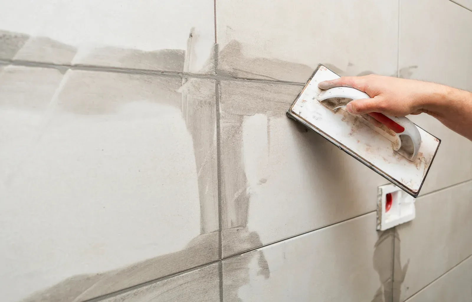 A person is using a trowel on a tiled wall.